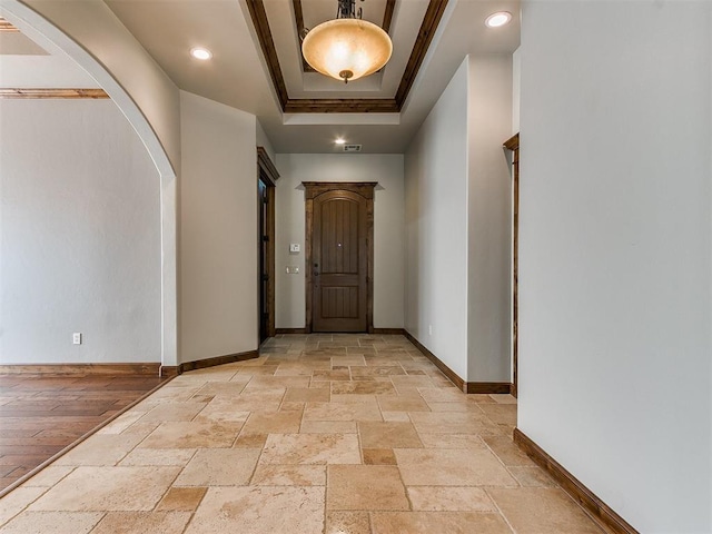 entrance foyer with stone tile floors, visible vents, baseboards, a raised ceiling, and arched walkways