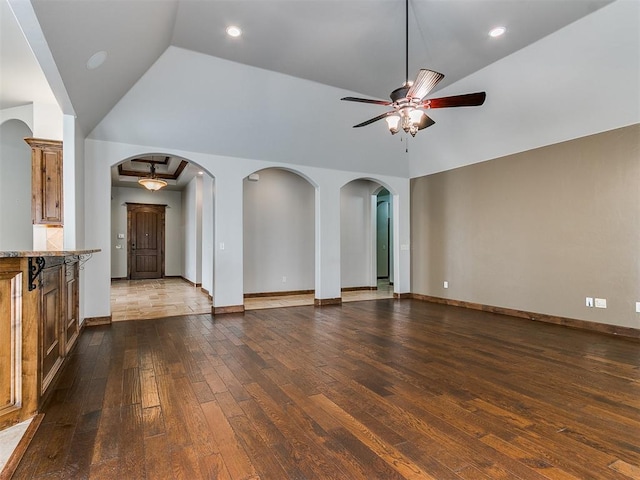 unfurnished living room featuring baseboards, arched walkways, dark wood finished floors, and a ceiling fan