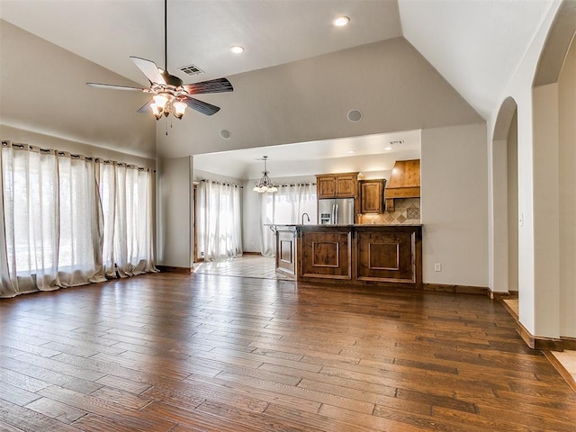 unfurnished living room featuring dark wood-style flooring, visible vents, high vaulted ceiling, baseboards, and ceiling fan with notable chandelier