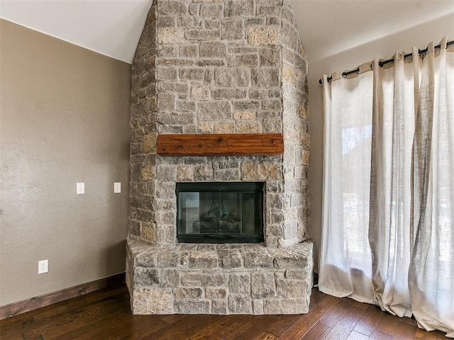 unfurnished living room with a textured wall, wood-type flooring, vaulted ceiling, and a stone fireplace