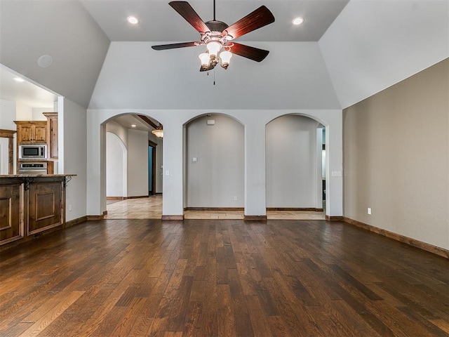 unfurnished living room with arched walkways, hardwood / wood-style floors, a ceiling fan, high vaulted ceiling, and baseboards