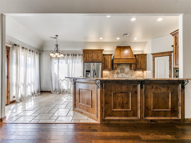 kitchen with hardwood / wood-style flooring, stainless steel appliances, visible vents, backsplash, and custom exhaust hood