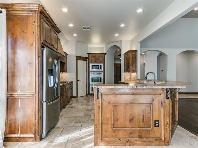 kitchen featuring arched walkways, stone tile floors, visible vents, appliances with stainless steel finishes, and decorative backsplash