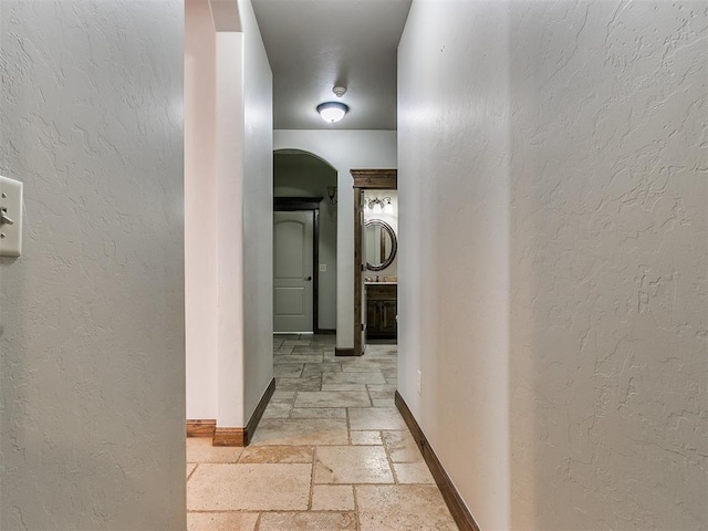 hallway featuring stone tile flooring, a textured wall, and baseboards