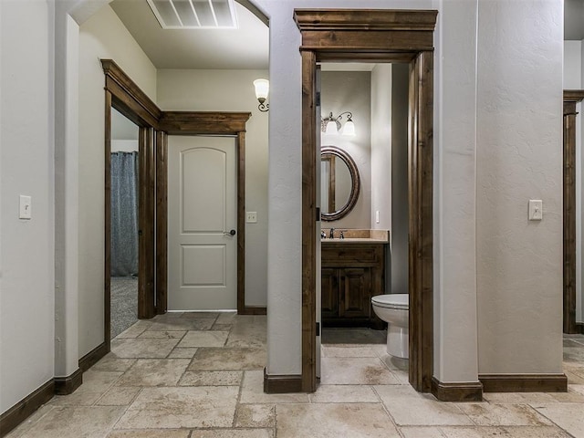 full bath with stone tile floors, visible vents, baseboards, toilet, and vanity