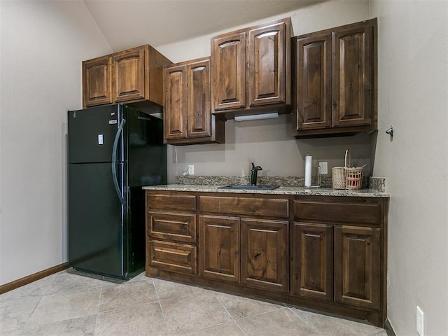 kitchen with light stone counters, a sink, baseboards, dark brown cabinets, and freestanding refrigerator