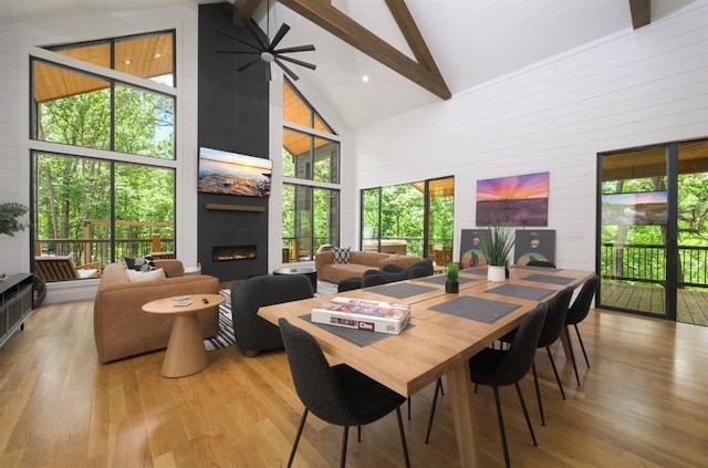 dining area with high vaulted ceiling, a large fireplace, beam ceiling, and wood finished floors