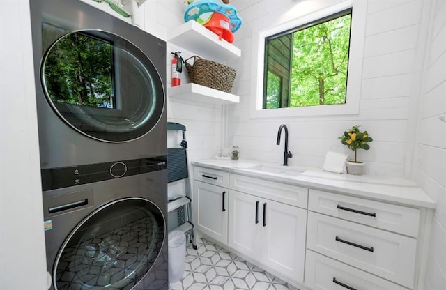 laundry room featuring cabinet space, a sink, and stacked washer and clothes dryer