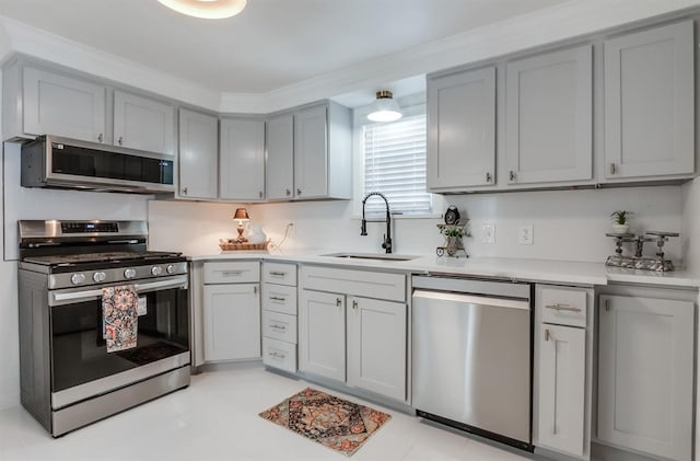 kitchen with light countertops, stainless steel appliances, a sink, and gray cabinetry