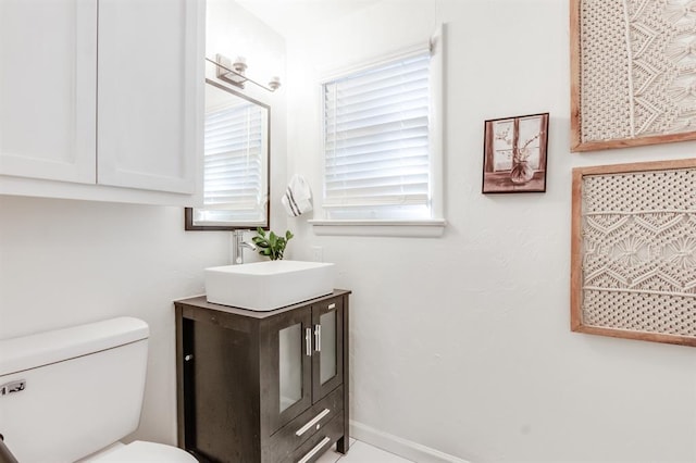 half bath with toilet, plenty of natural light, baseboards, and vanity