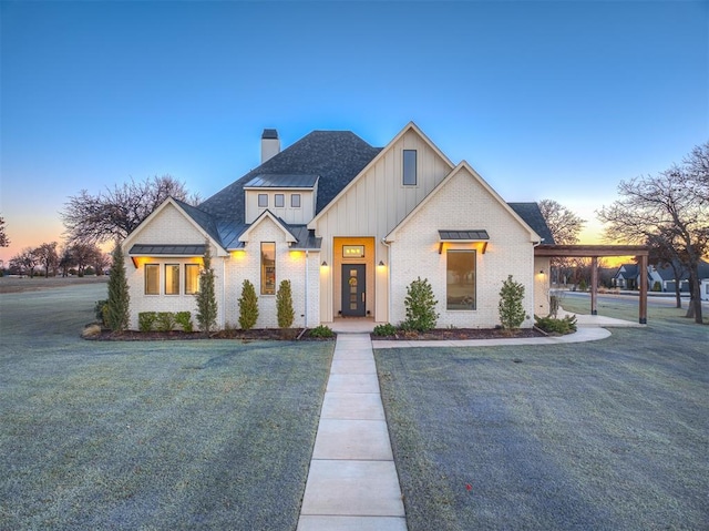 modern farmhouse style home with brick siding, a chimney, board and batten siding, a front yard, and a standing seam roof