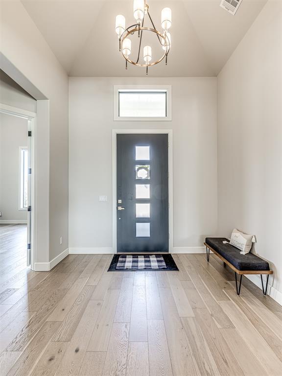 entryway featuring light wood-type flooring, a notable chandelier, lofted ceiling, and baseboards