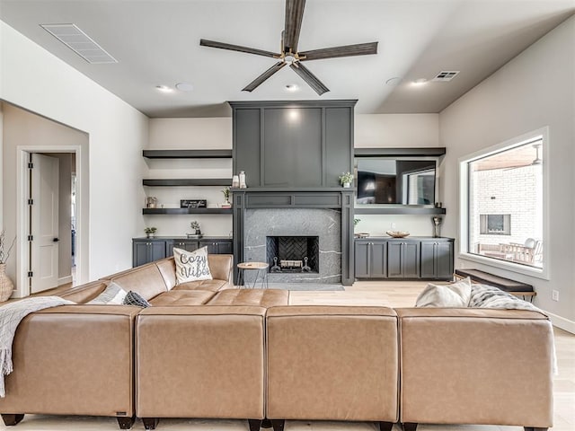 living area with a large fireplace, ceiling fan, light wood-type flooring, and visible vents