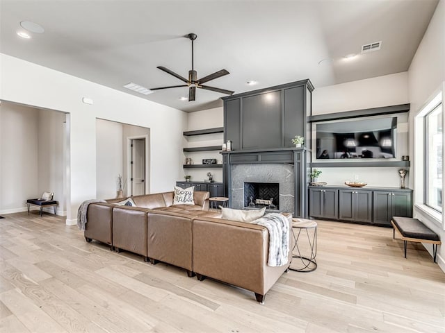 living area featuring light wood-type flooring, a premium fireplace, visible vents, and a ceiling fan