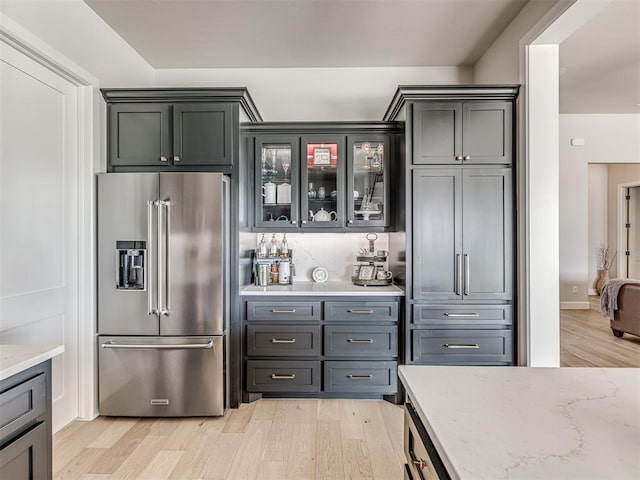 kitchen with light stone countertops, light wood finished floors, glass insert cabinets, and high end fridge