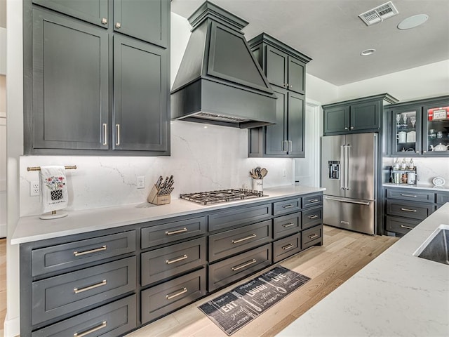 kitchen with visible vents, decorative backsplash, appliances with stainless steel finishes, light wood-type flooring, and premium range hood