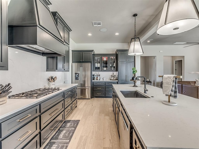 kitchen with light wood finished floors, visible vents, appliances with stainless steel finishes, a sink, and premium range hood