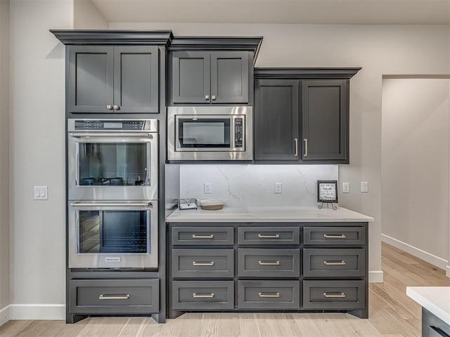 kitchen with light countertops, decorative backsplash, appliances with stainless steel finishes, light wood-style floors, and baseboards