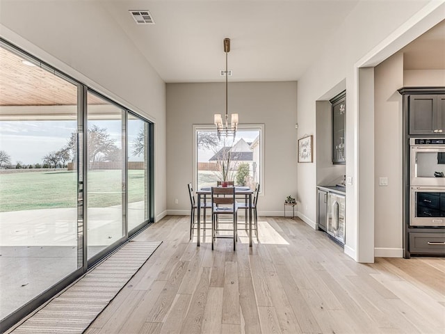 unfurnished dining area with light wood finished floors, visible vents, a chandelier, beverage cooler, and baseboards