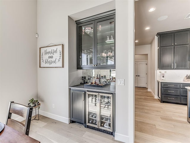 bar featuring a bar, light wood-style flooring, wine cooler, and backsplash