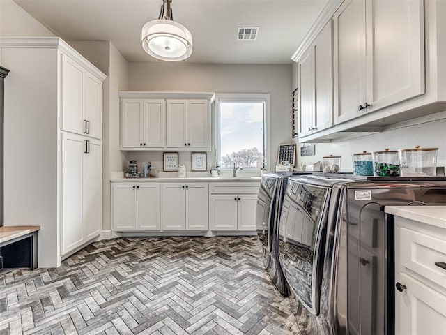 clothes washing area with brick floor, separate washer and dryer, a sink, visible vents, and cabinet space