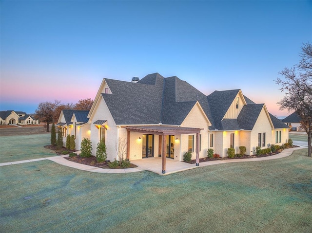 exterior space with board and batten siding, a shingled roof, a lawn, and brick siding