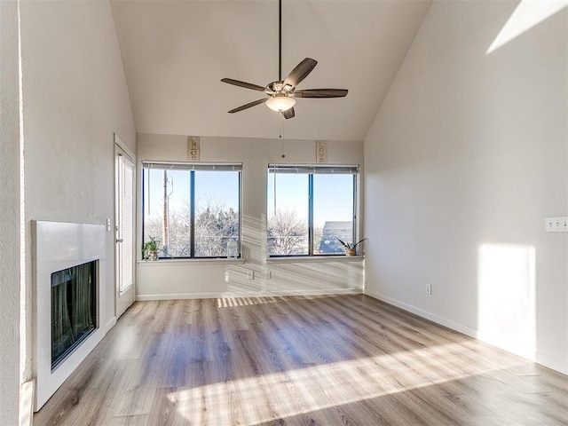 unfurnished living room with baseboards, a ceiling fan, wood finished floors, a fireplace, and high vaulted ceiling