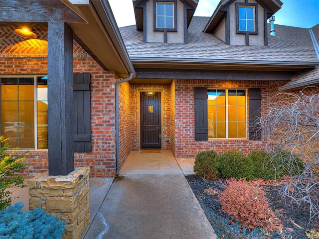 doorway to property with brick siding and roof with shingles