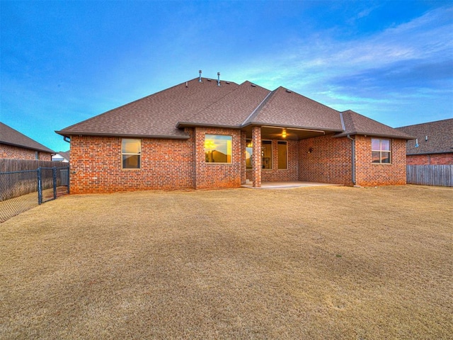 rear view of house with a patio area, brick siding, a fenced backyard, and roof with shingles