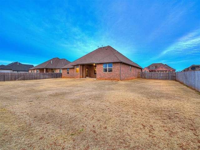 back of house with a fenced backyard, a lawn, and brick siding