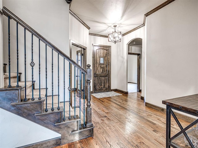 foyer with arched walkways, crown molding, wood finished floors, a chandelier, and stairs