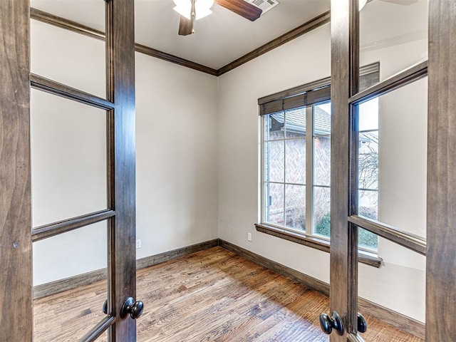 empty room with ornamental molding, wood finished floors, a ceiling fan, and baseboards