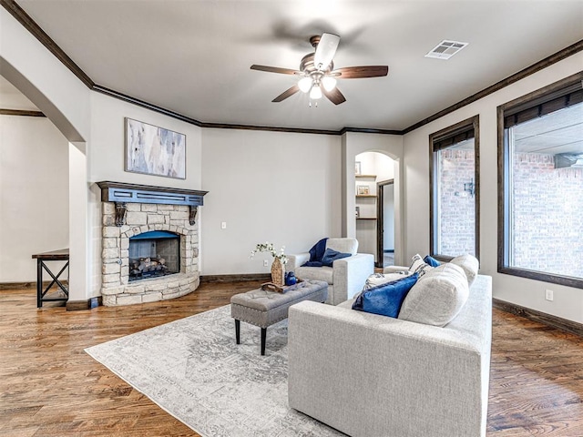 living area with arched walkways, a stone fireplace, wood finished floors, and visible vents