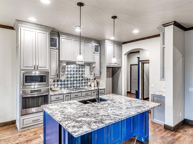 kitchen featuring stainless steel appliances, arched walkways, a sink, and light wood-style flooring