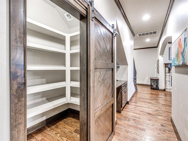 spacious closet with arched walkways, a barn door, wood finished floors, and visible vents