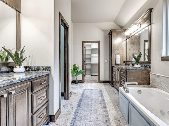 bathroom with baseboards, two vanities, a whirlpool tub, vaulted ceiling, and a sink