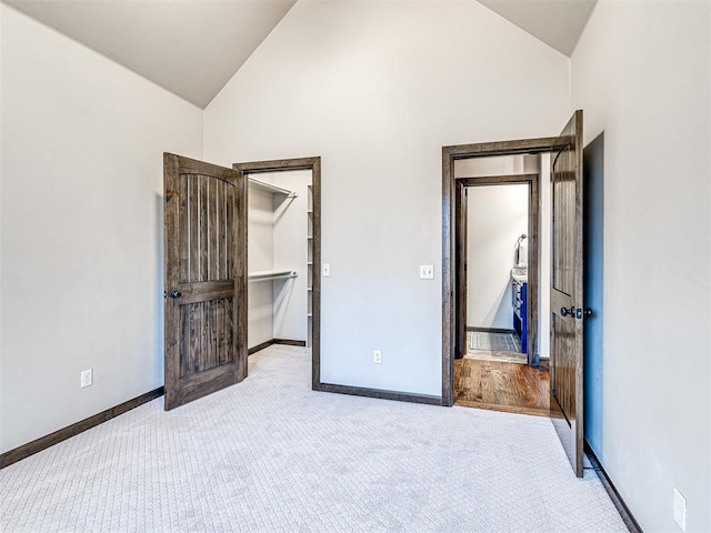 unfurnished bedroom with high vaulted ceiling, carpet, a spacious closet, and baseboards