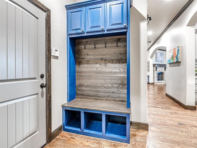 mudroom featuring light wood-style flooring, baseboards, and a fireplace with raised hearth