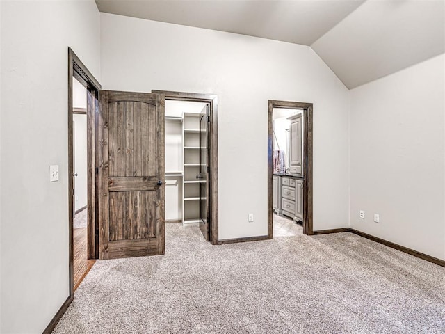 unfurnished bedroom with carpet floors, a walk in closet, lofted ceiling, a closet, and baseboards