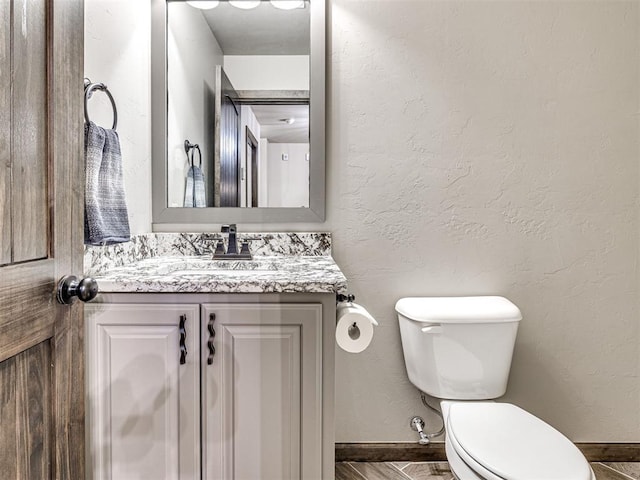 bathroom with a textured wall, vanity, toilet, and baseboards