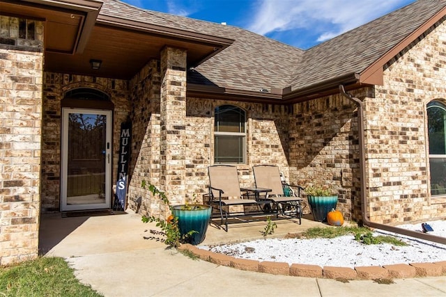 view of exterior entry with a shingled roof and brick siding