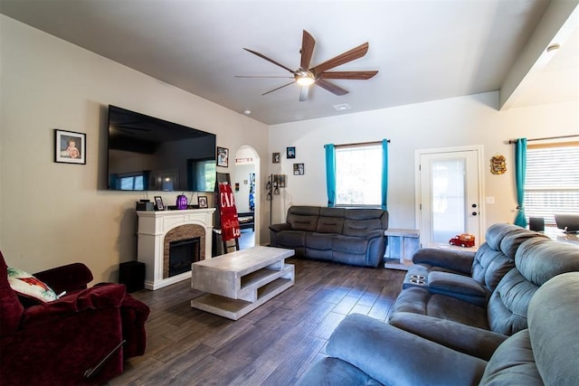 living room with ceiling fan, a fireplace, arched walkways, and dark wood-type flooring