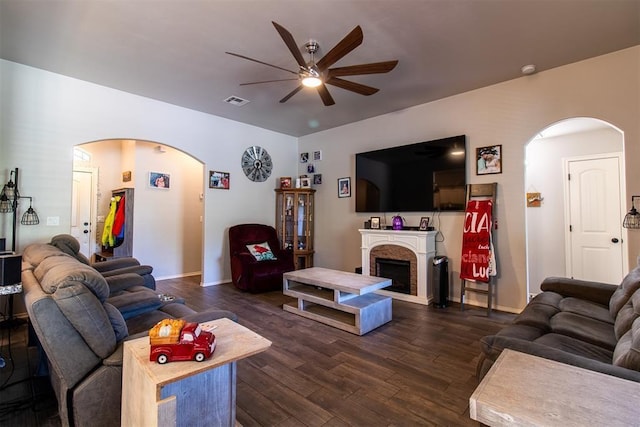 living room featuring ceiling fan, a fireplace, arched walkways, and dark wood finished floors