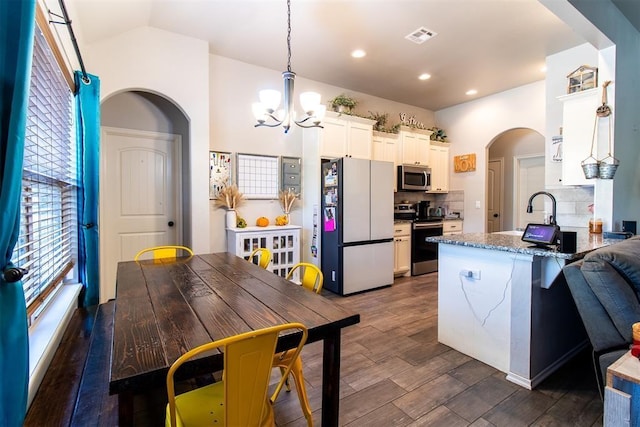 kitchen with stainless steel appliances, arched walkways, dark wood-type flooring, and tasteful backsplash