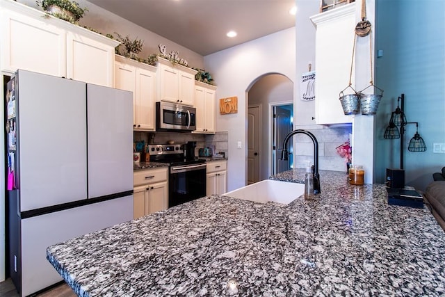 kitchen with arched walkways, stainless steel appliances, a sink, dark stone counters, and a peninsula