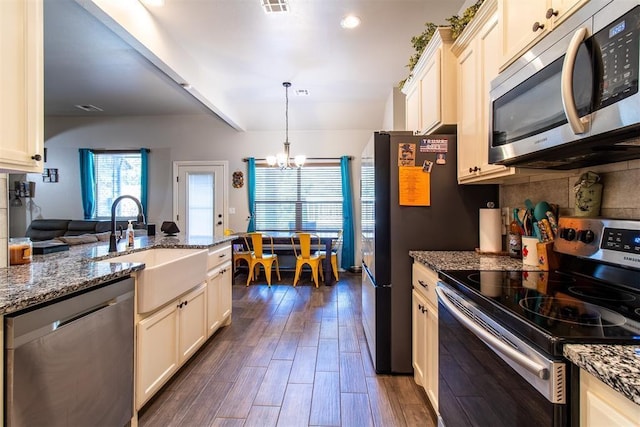 kitchen with a notable chandelier, dark wood-type flooring, a sink, appliances with stainless steel finishes, and dark stone countertops