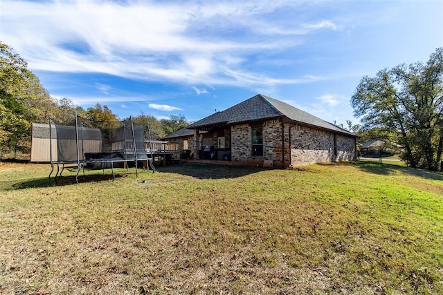 view of property exterior with a trampoline, brick siding, a yard, and an outdoor structure