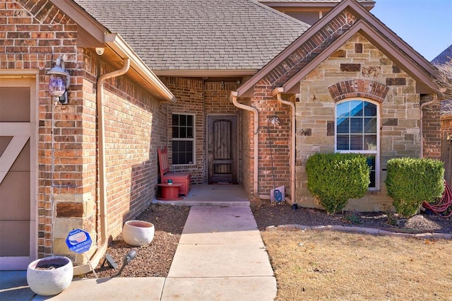 view of exterior entry with a shingled roof, stone siding, and brick siding