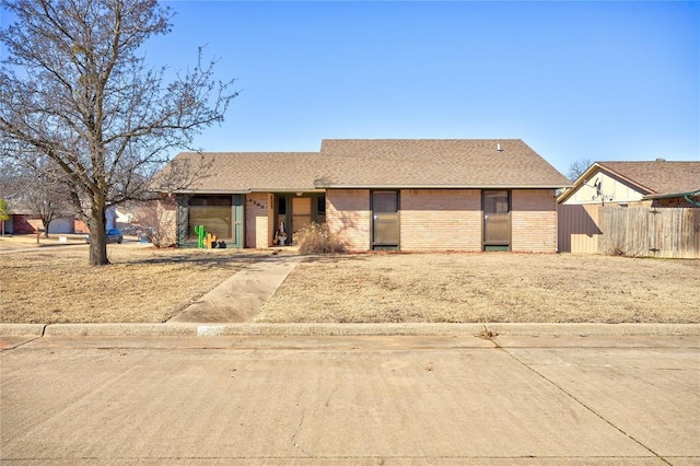 single story home with a shingled roof, brick siding, and fence