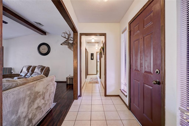 corridor with light tile patterned floors, lofted ceiling with beams, visible vents, and baseboards